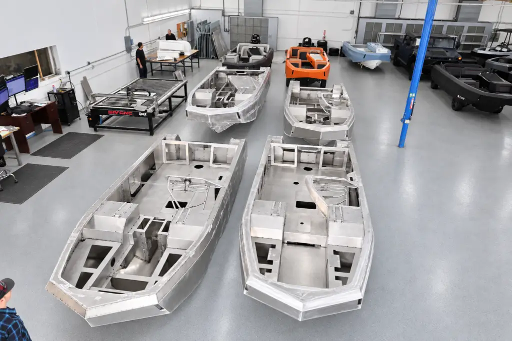 Four unfinished aluminum WaterCar hulls on the workshop floor, with completed vehicles behind them.