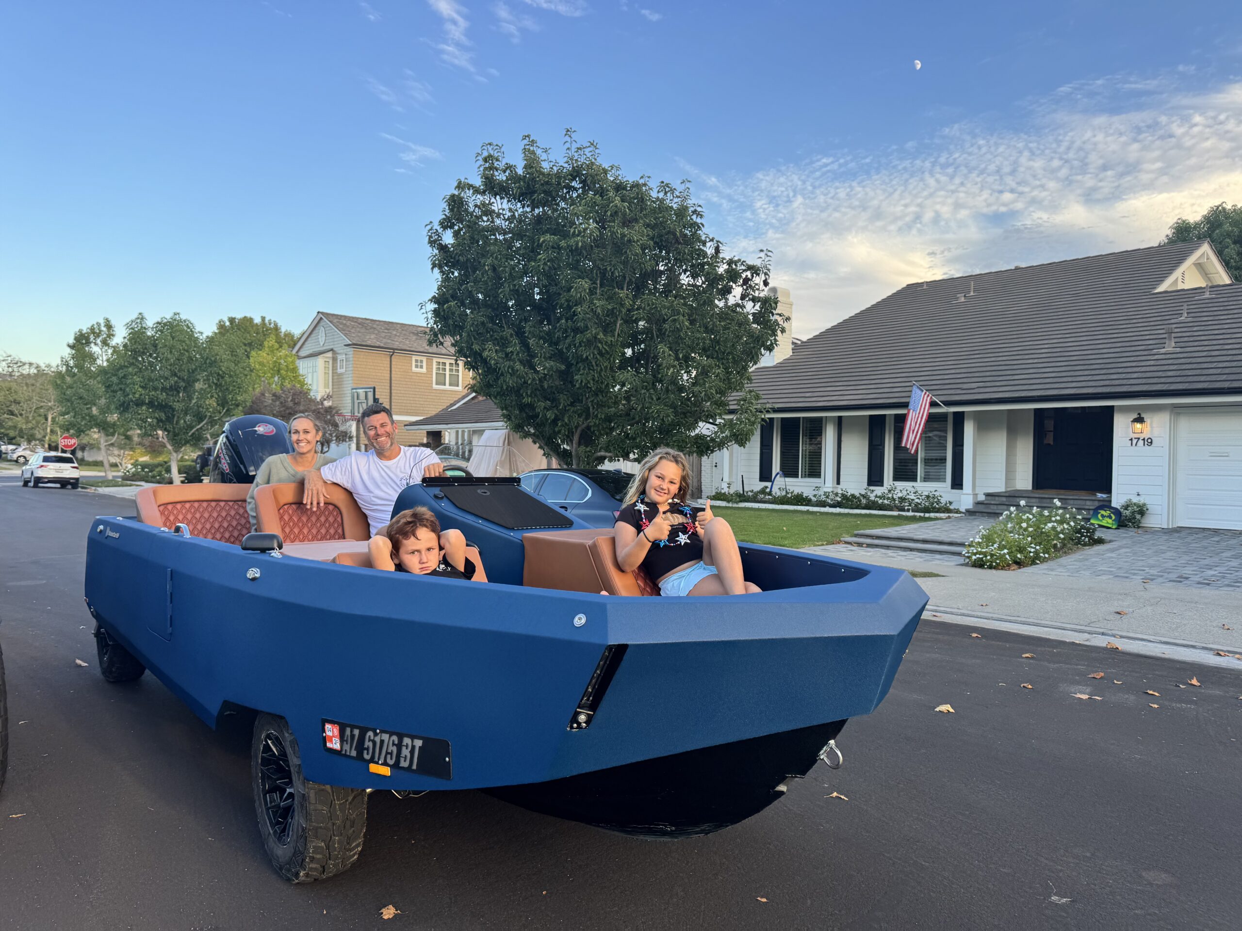 Family seated in a blue WaterCar with orange upholstery on a neighborhood street.