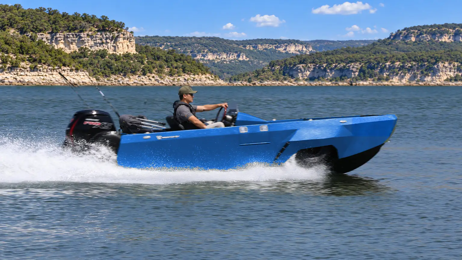 A blue WaterCar Adventure cruises past limestone bluffs with spray alongside the hull.